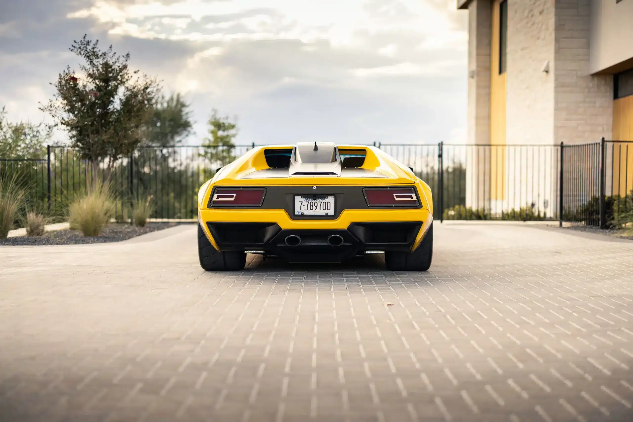 Heckansicht des gelben DeTomaso Pantera ADRNLN mit breiter Karosserie und markantem Diffusor auf einer Einfahrt.