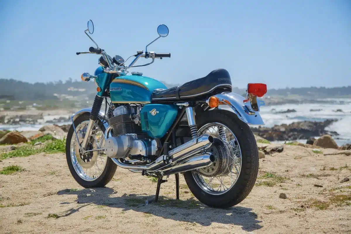 Seitenansicht eines Honda CB750 Prototyps von 1968 in Türkis mit verchromten Details, stehend am Strand mit Meeresblick.