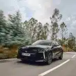 Schwarzer DS N°4 fährt dynamisch auf einer Landstraße durch bewaldete Landschaft.