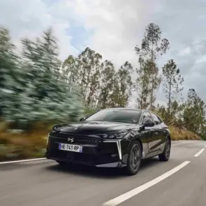 Schwarzer DS N°4 fährt dynamisch auf einer Landstraße durch bewaldete Landschaft.