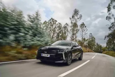 Schwarzer DS N°4 fährt dynamisch auf einer Landstraße durch bewaldete Landschaft.