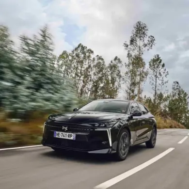 Schwarzer DS N°4 fährt dynamisch auf einer Landstraße durch bewaldete Landschaft.