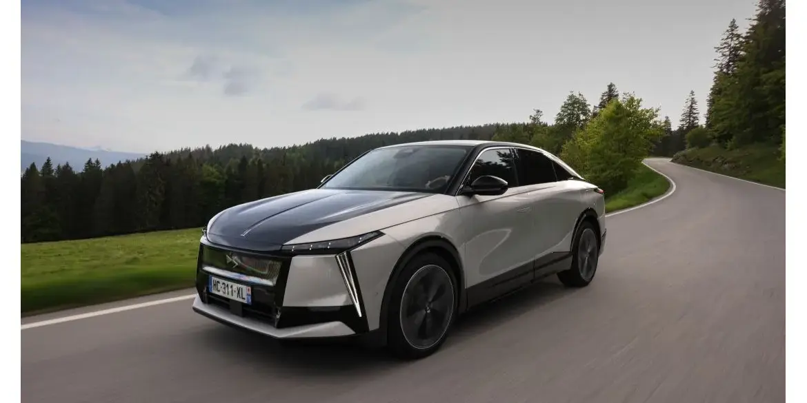 DS N°8 Elektrofahrzeug fährt dynamisch auf einer Landstraße durch eine grüne, bewaldete Landschaft.