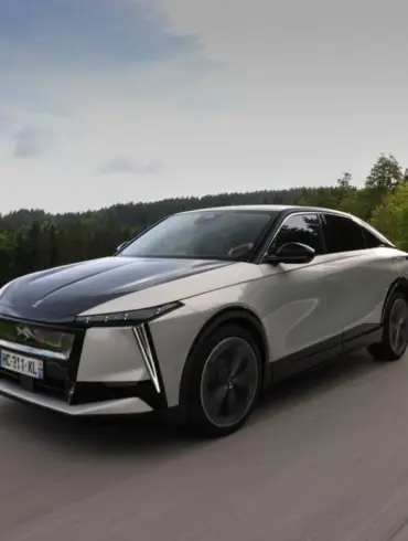 DS N°8 Elektrofahrzeug fährt dynamisch auf einer Landstraße durch eine grüne, bewaldete Landschaft.