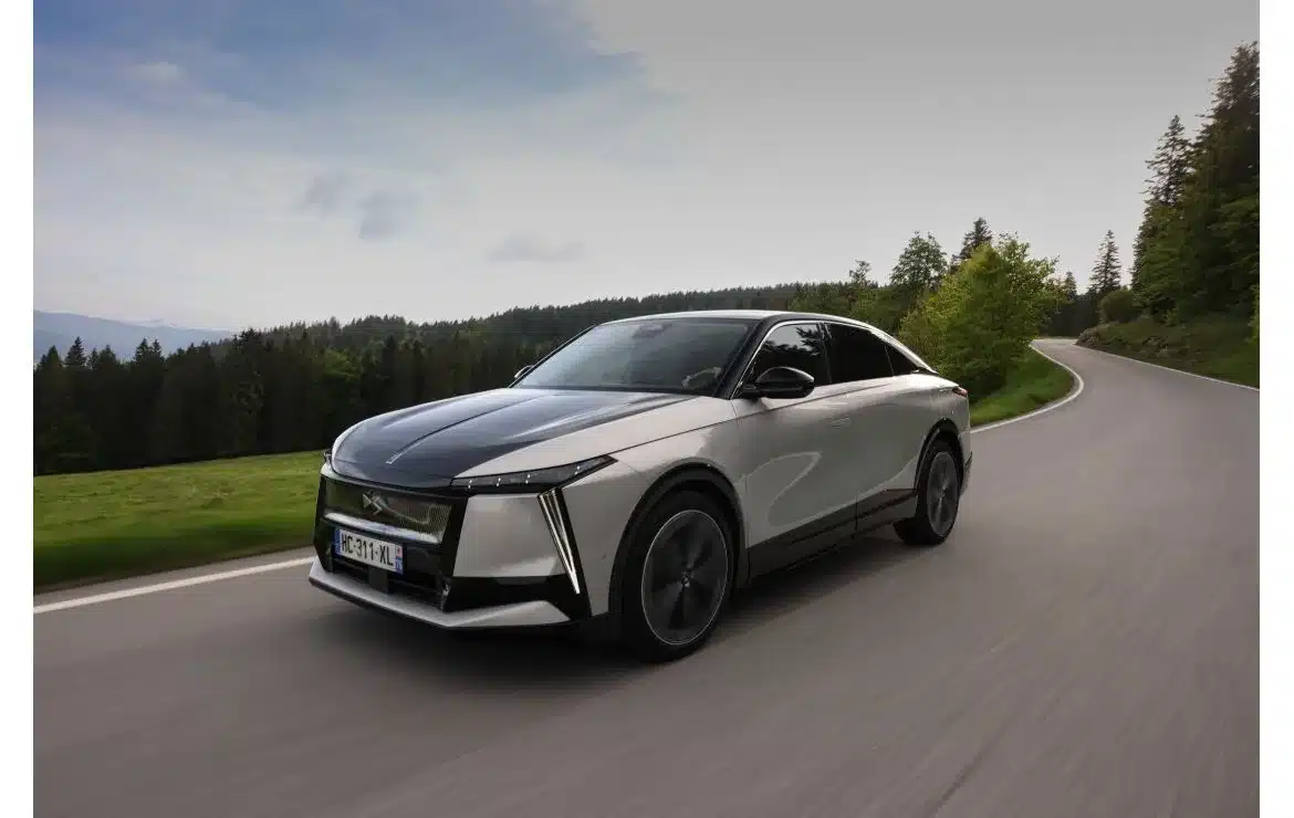 DS N°8 Elektrofahrzeug fährt dynamisch auf einer Landstraße durch eine grüne, bewaldete Landschaft.