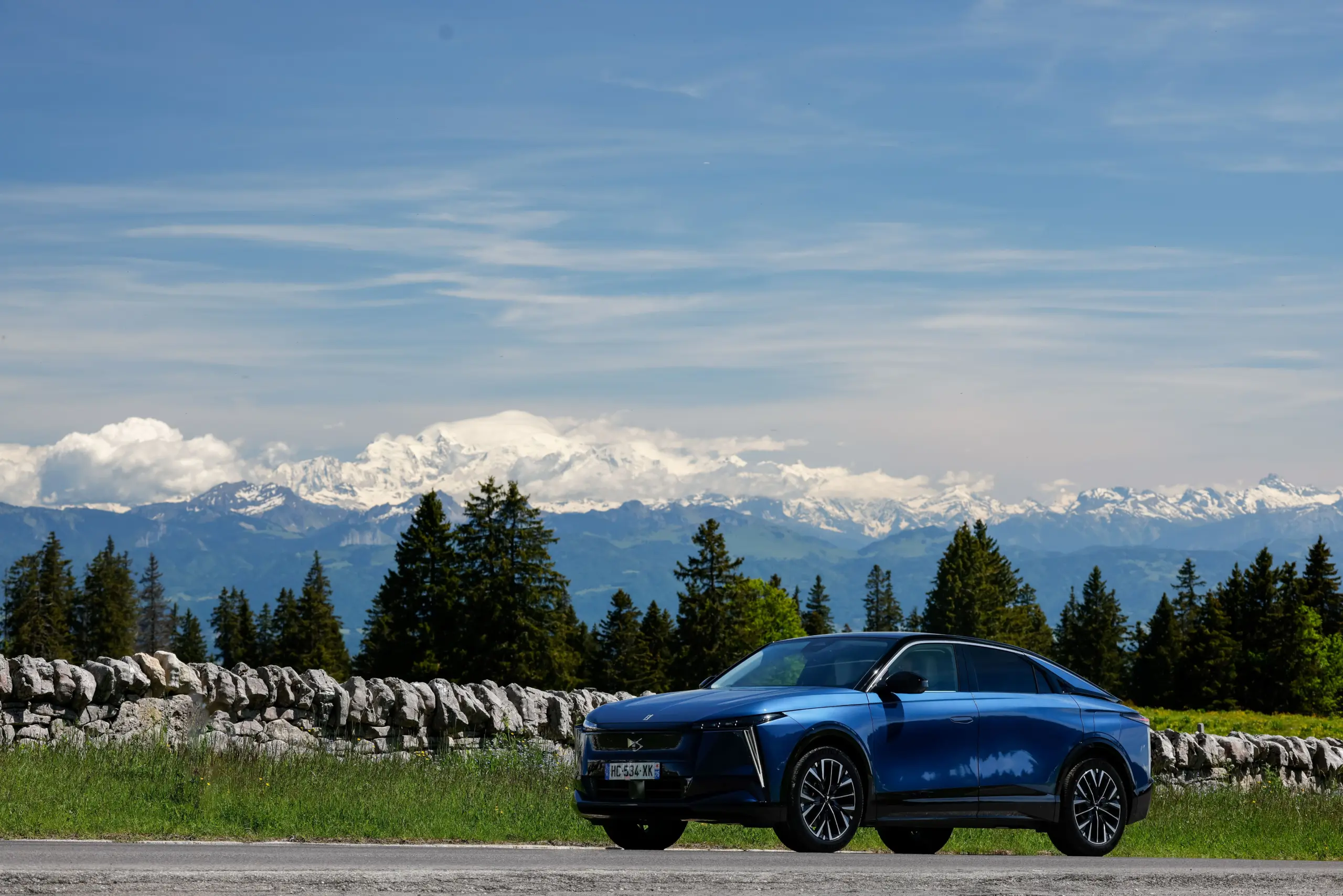 Blauer DS N°8 Elektro-SUV steht vor einer Steinmauer mit Alpen im Hintergrund