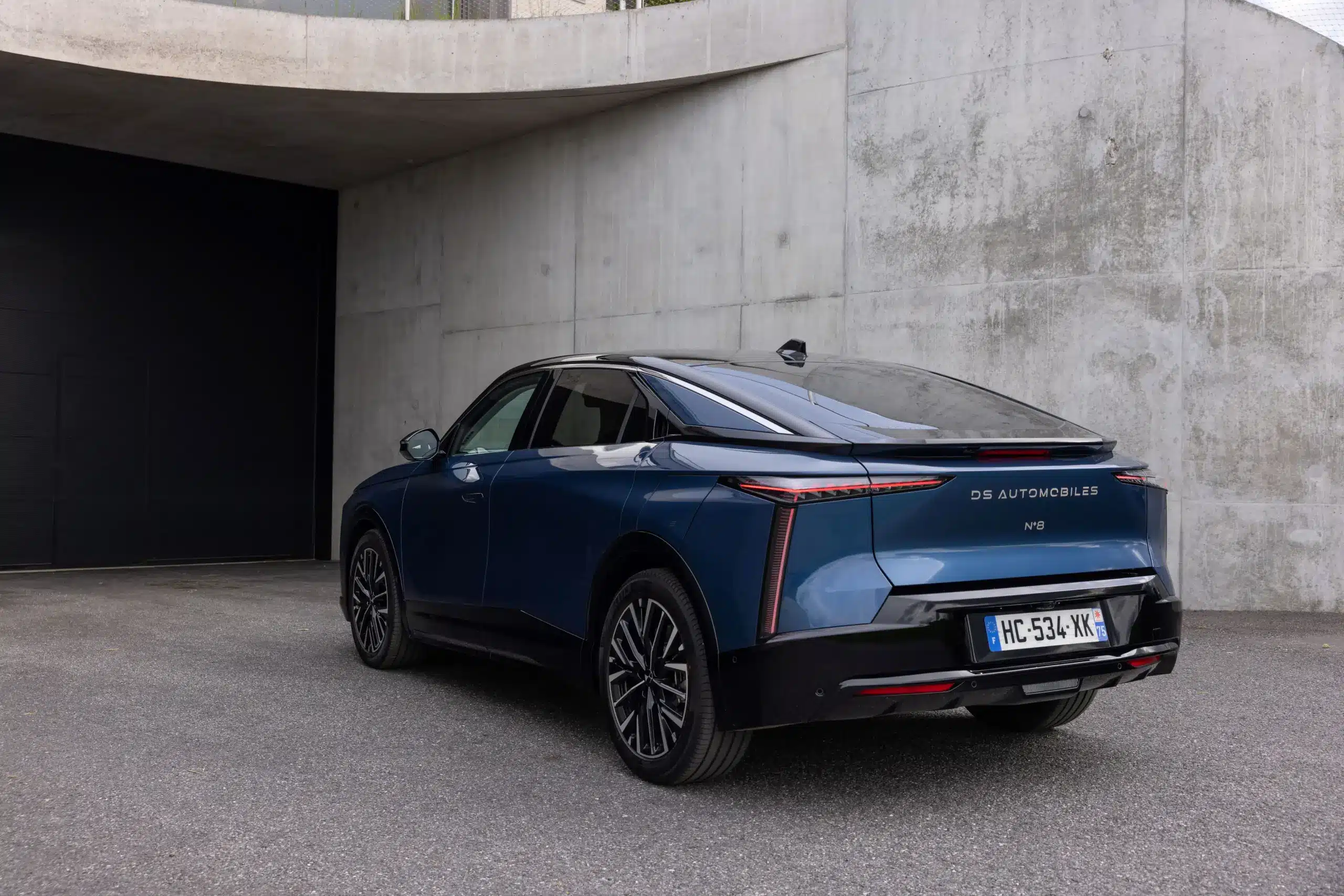 Heckansicht des elektrischen DS N°8 SUV-Coupés in Blau, vor Betonwand geparkt.