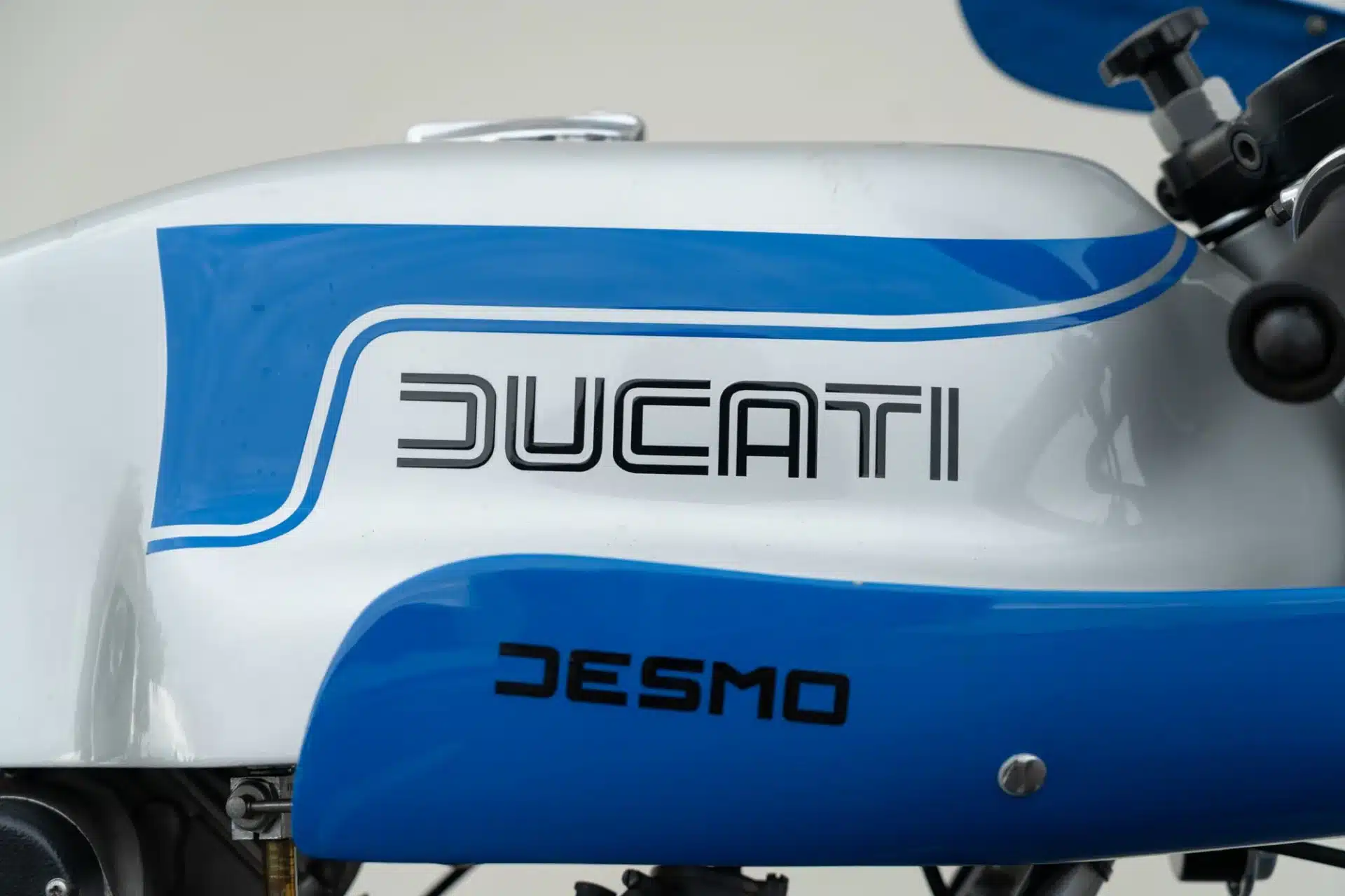 Nahaufnahme des Tanks einer 1975 Ducati 900 Super Sport mit blauem Ducati-Schriftzug und Desmo-Logo.