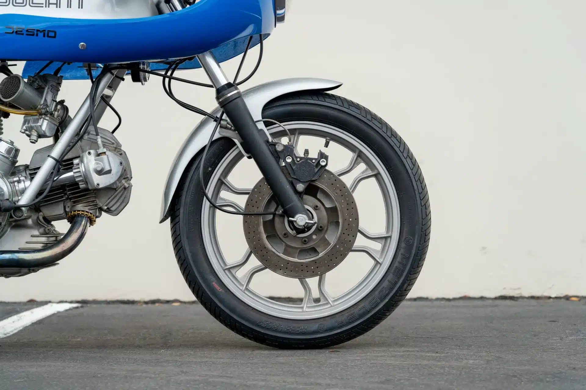 Nahaufnahme des Vorderrads einer blauen Ducati 900 Super Sport von 1975 mit Bremsscheibe und Sicht auf den Motorblock.