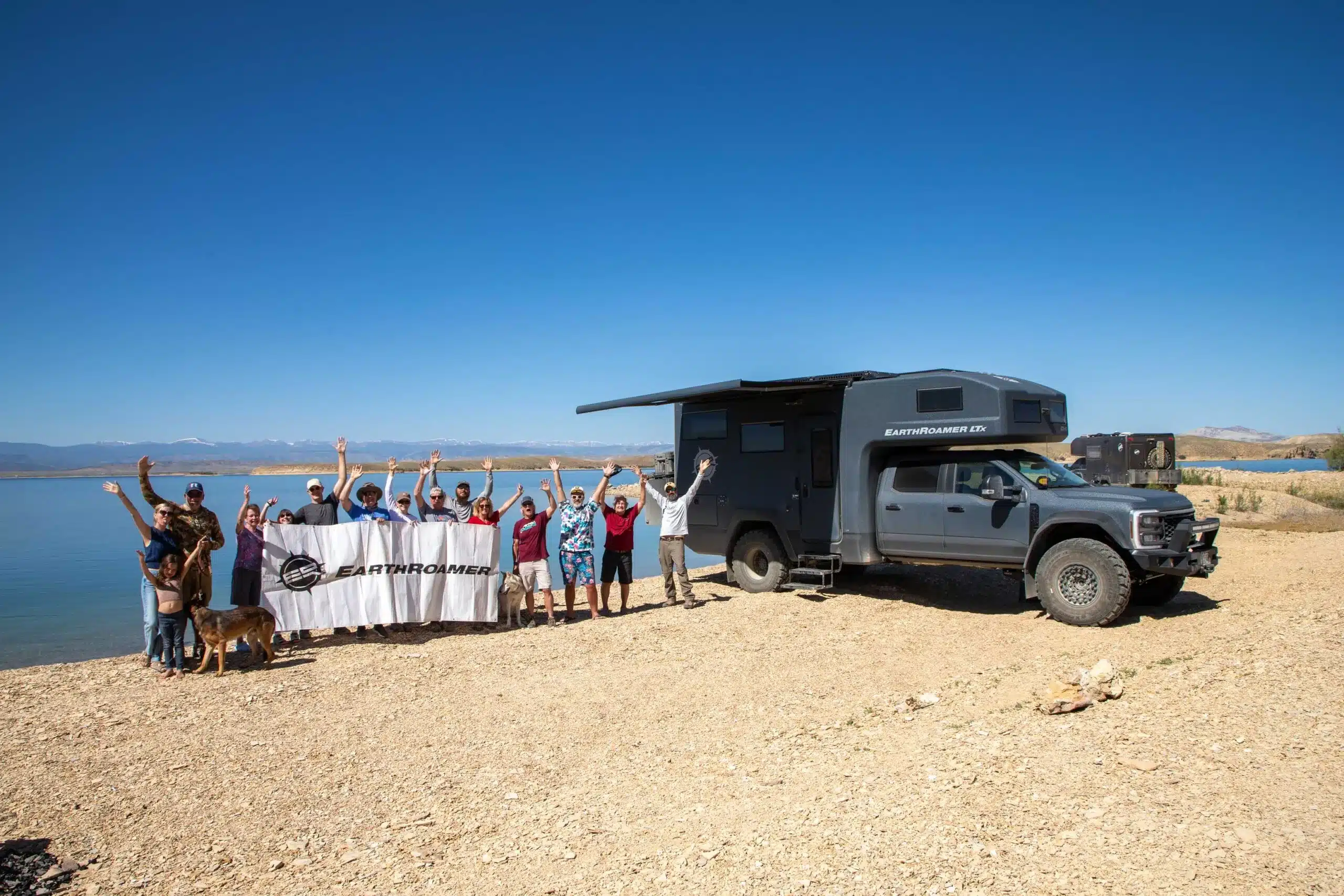 EarthRoamer SX Explore Expeditionsmobil mit Gruppe am Seeufer unter blauem Himmel