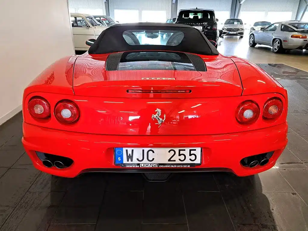 Heckansicht eines roten Ferrari 360 Spider mit schwarzem Verdeck und schwedischem Kennzeichen in einer Ausstellungshalle.