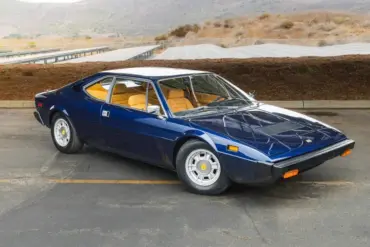 Seitenansicht eines Ferrari Dino 308 GT4 von 1975 in blauer Lackierung vor landschaftlicher Kulisse.