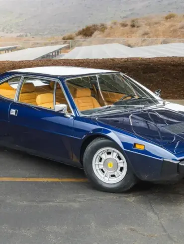 Seitenansicht eines Ferrari Dino 308 GT4 von 1975 in blauer Lackierung vor landschaftlicher Kulisse.
