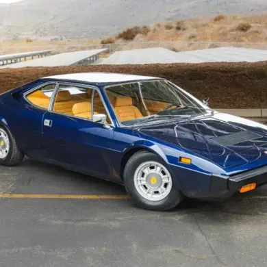 Seitenansicht eines Ferrari Dino 308 GT4 von 1975 in blauer Lackierung vor landschaftlicher Kulisse.