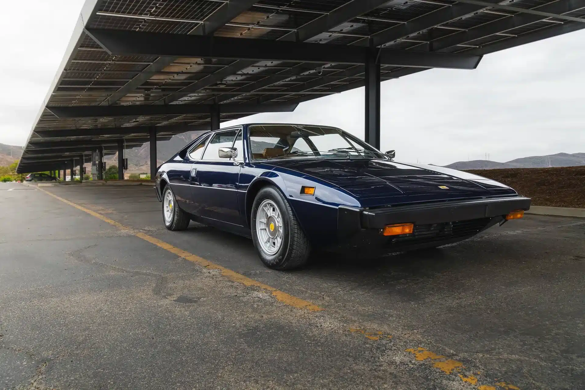 Ferrari Dino 308 GT4 von 1975, lackiert in Blu Le Mans, steht auf einem Parkplatz unter einer Photovoltaikanlage