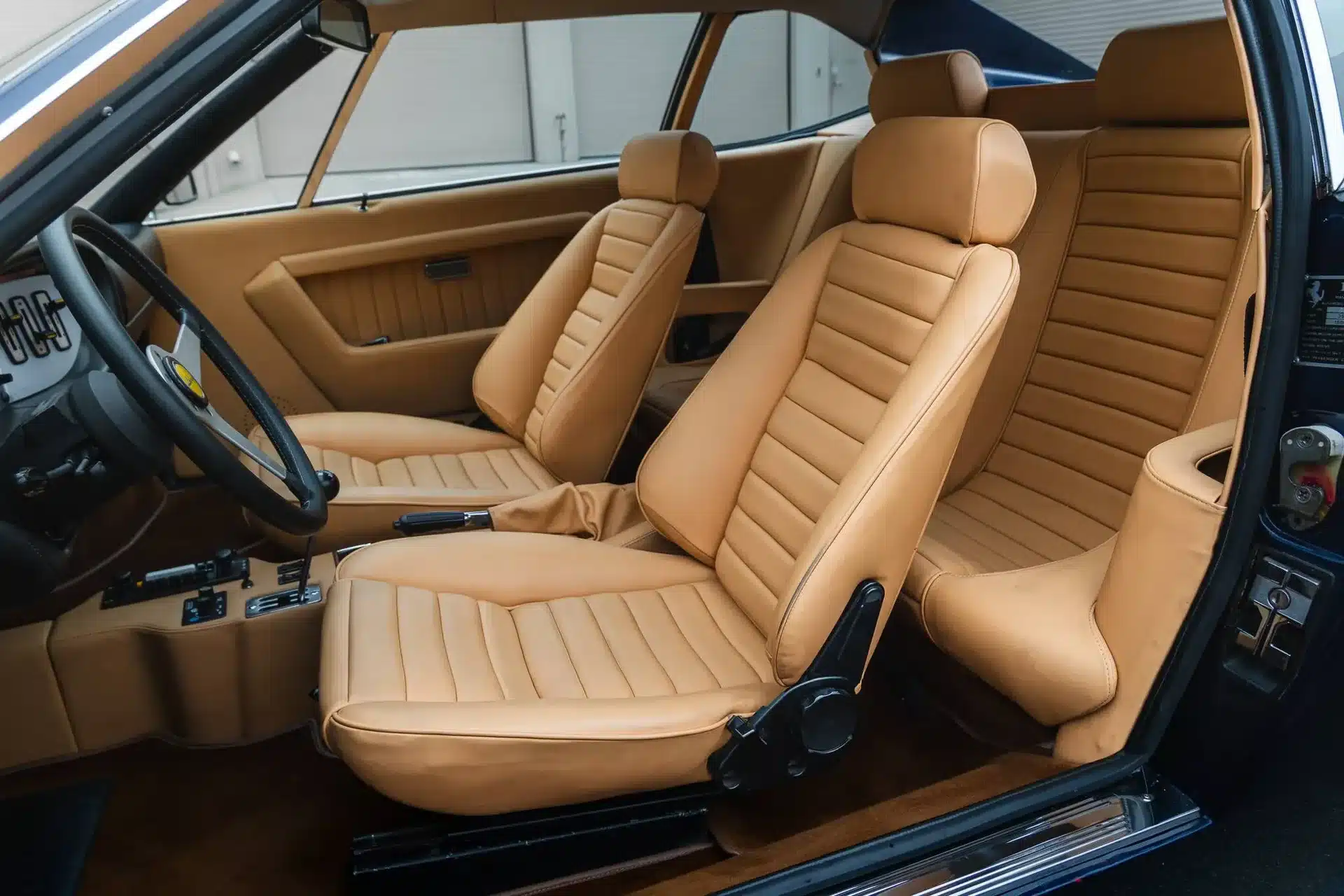 Innenraum eines Ferrari Dino 308 GT4 mit restaurierter, tanfarbener Lederausstattung und vorderen sowie hinteren Sitzen.