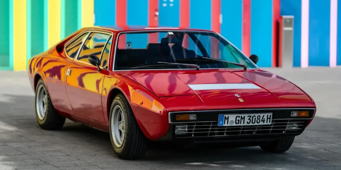 Roter Ferrari Dino 308 GT4 von 1975, geparkt vor bunter Wand, deutsche H-Zulassung