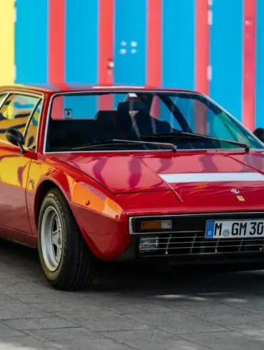 Roter Ferrari Dino 308 GT4 von 1975, geparkt vor bunter Wand, deutsche H-Zulassung