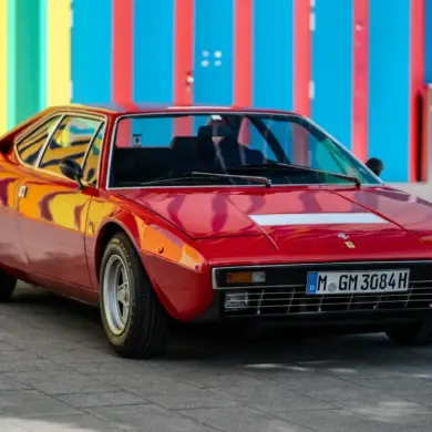Roter Ferrari Dino 308 GT4 von 1975, geparkt vor bunter Wand, deutsche H-Zulassung