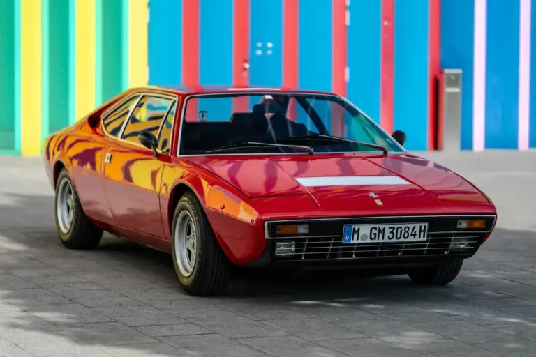 Roter Ferrari Dino 308 GT4 von 1975, geparkt vor bunter Wand, deutsche H-Zulassung