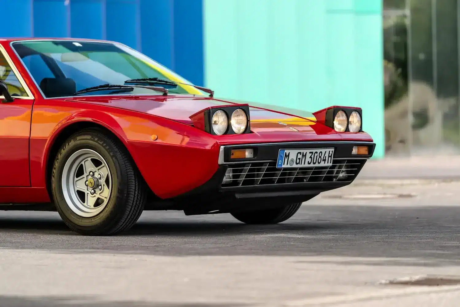 Roter Ferrari Dino 308 GT4 aus dem Jahr 1975 mit hochgeklappten Scheinwerfern, fotografiert von vorne seitlich.