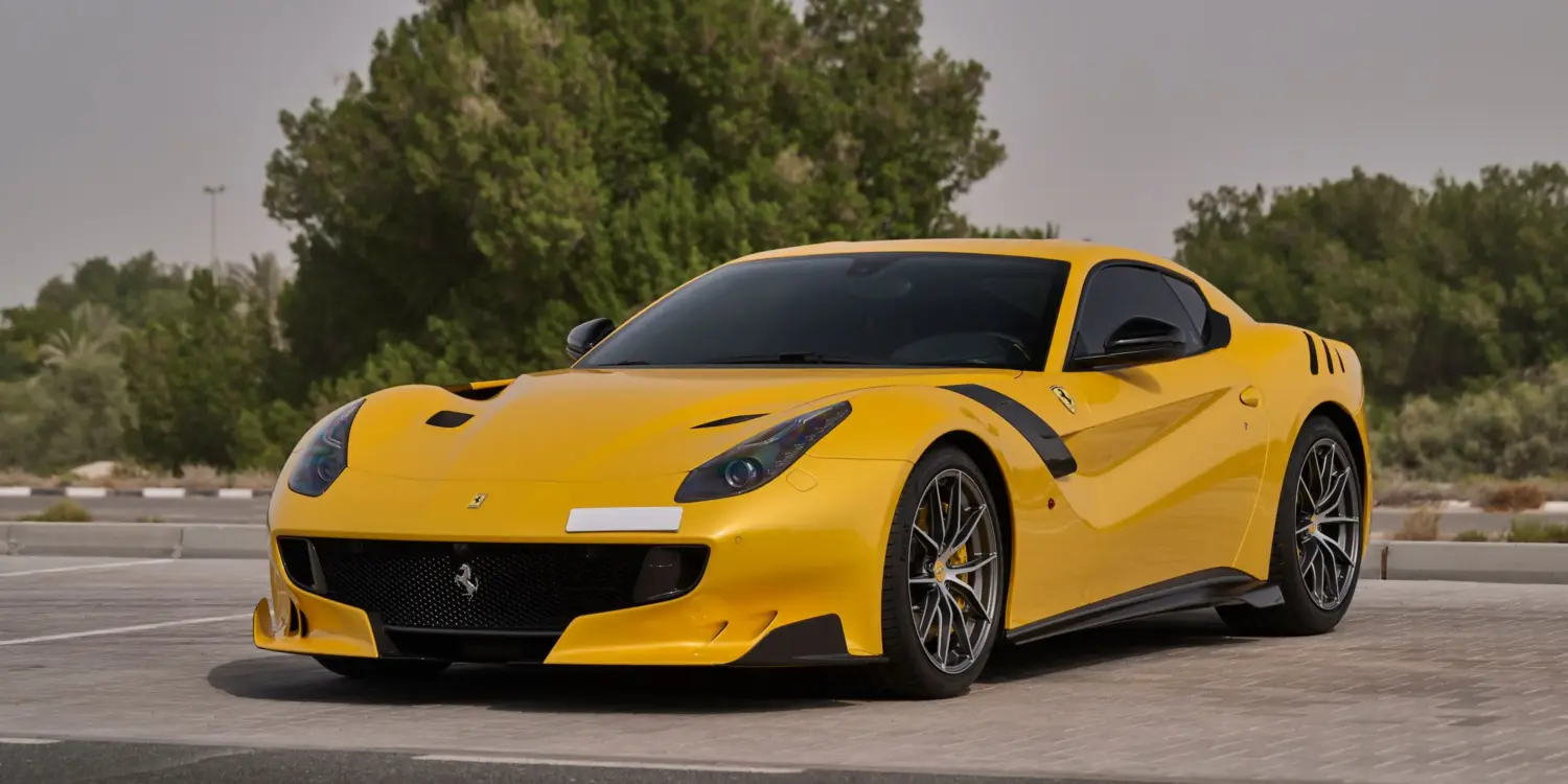 Gelber Ferrari F12 TDF mit Carbon-Details auf einem Parkplatz, sportliches Erscheinungsbild, Frontansicht.