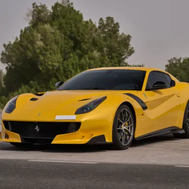 Gelber Ferrari F12 TDF mit Carbon-Details auf einem Parkplatz, sportliches Erscheinungsbild, Frontansicht.
