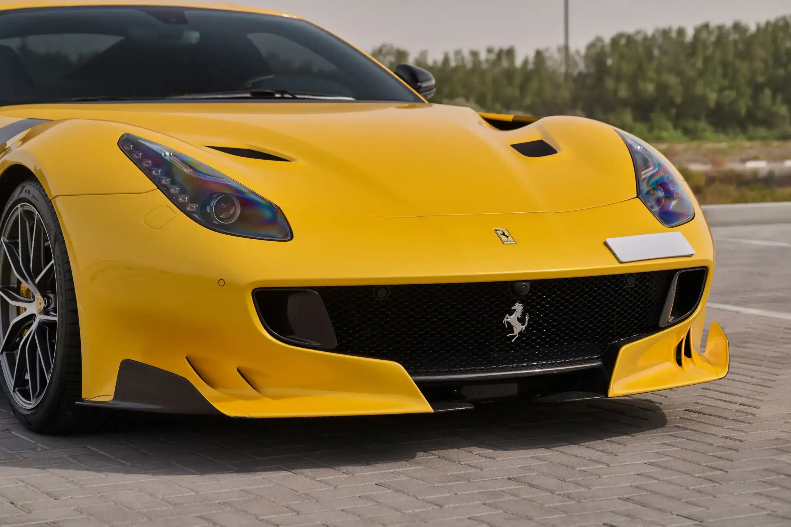 Ferrari F12 TDF in gelb, Frontpartie mit Carbon-Frontsplitter und sichtbaren Aerodynamikteilen auf einem Parkplatz