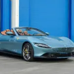 Ferrari Roma Spider 2025 in Celeste Trevi mit offenem Dach und braunem Lederinterieur, Seitenansicht.