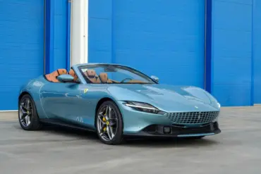 Ferrari Roma Spider 2025 in Celeste Trevi mit offenem Dach und braunem Lederinterieur, Seitenansicht.