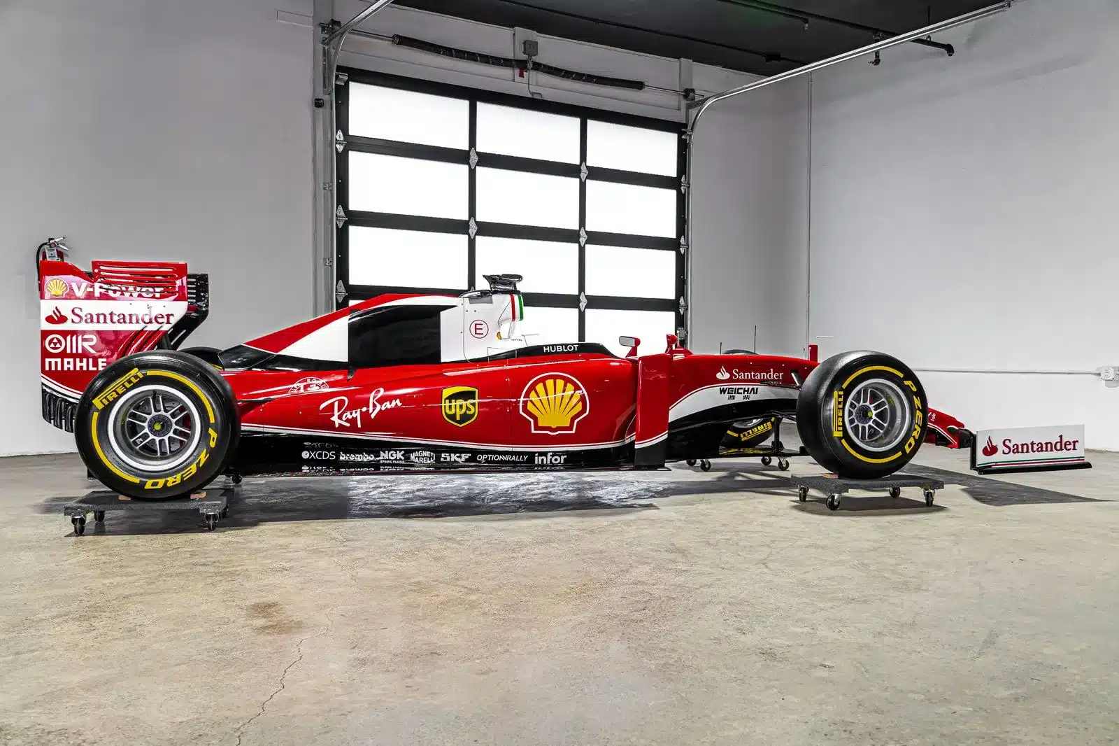 Seitenansicht einer Ferrari SF16-H Formel-1-Replika im Maßstab 1:1 auf Rollbrettern in einer hellen Halle.