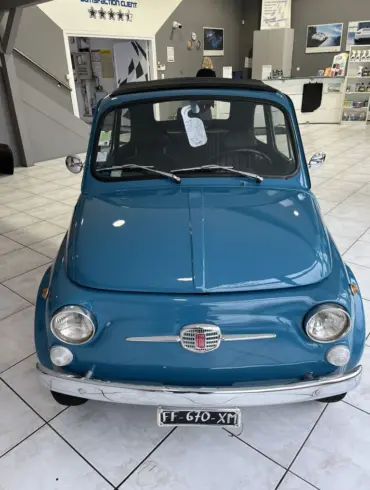 Blauer Fiat 500L Lusso von 1968 mit Faltdach, fotografiert frontal in einem hellen Showroom.