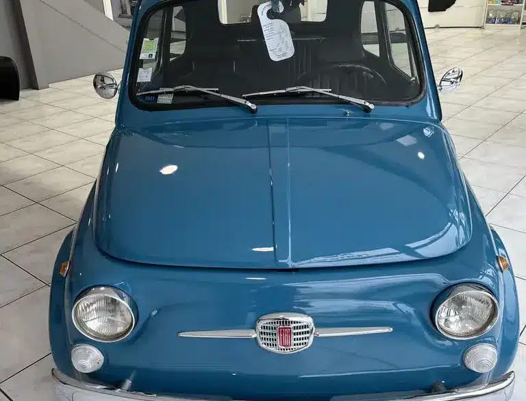 Blauer Fiat 500L Lusso von 1968 mit Faltdach, fotografiert frontal in einem hellen Showroom.