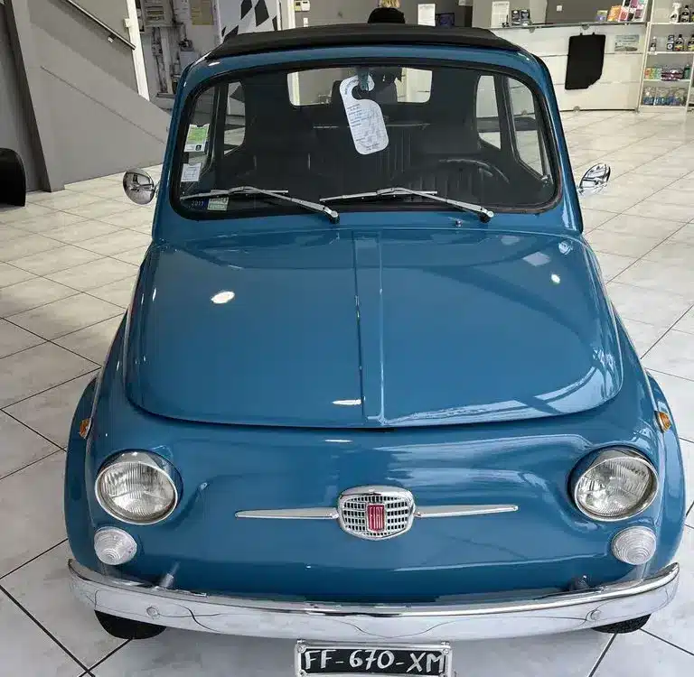 Blauer Fiat 500L Lusso von 1968 mit Faltdach, fotografiert frontal in einem hellen Showroom.