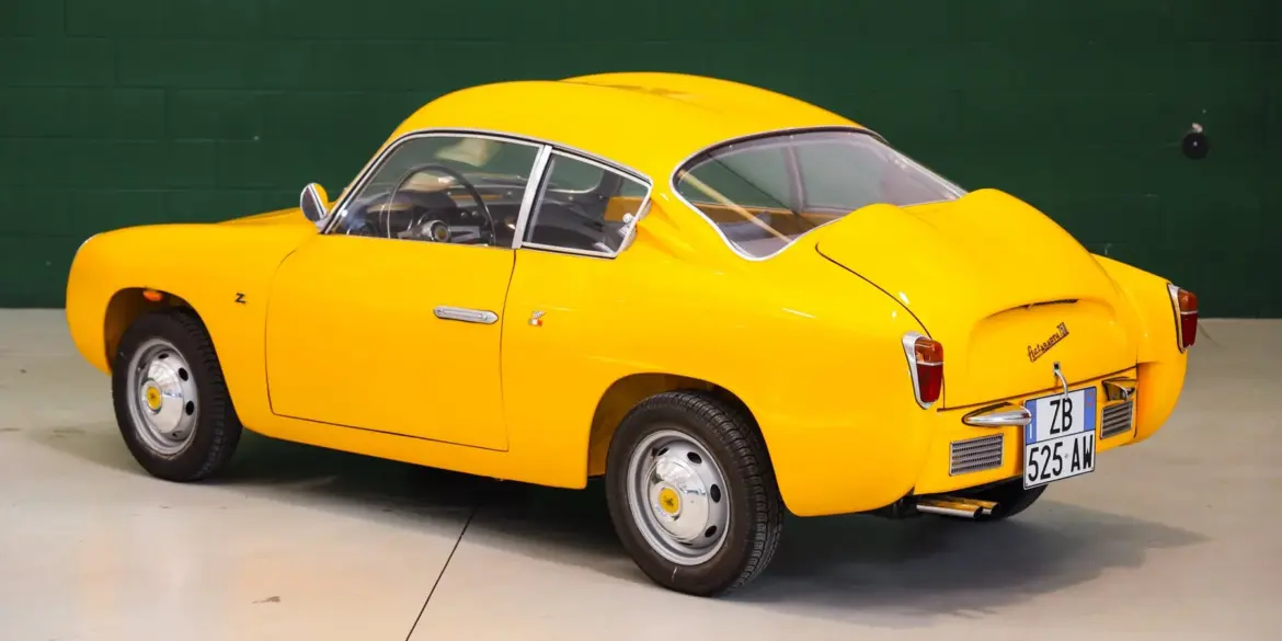 Fiat Abarth 750 Zagato, Baujahr 1958, gelb lackiert, restauriert, mit Double-Bubble-Dach, Seiten- und Heckansicht, aufgenommen in einer Halle.