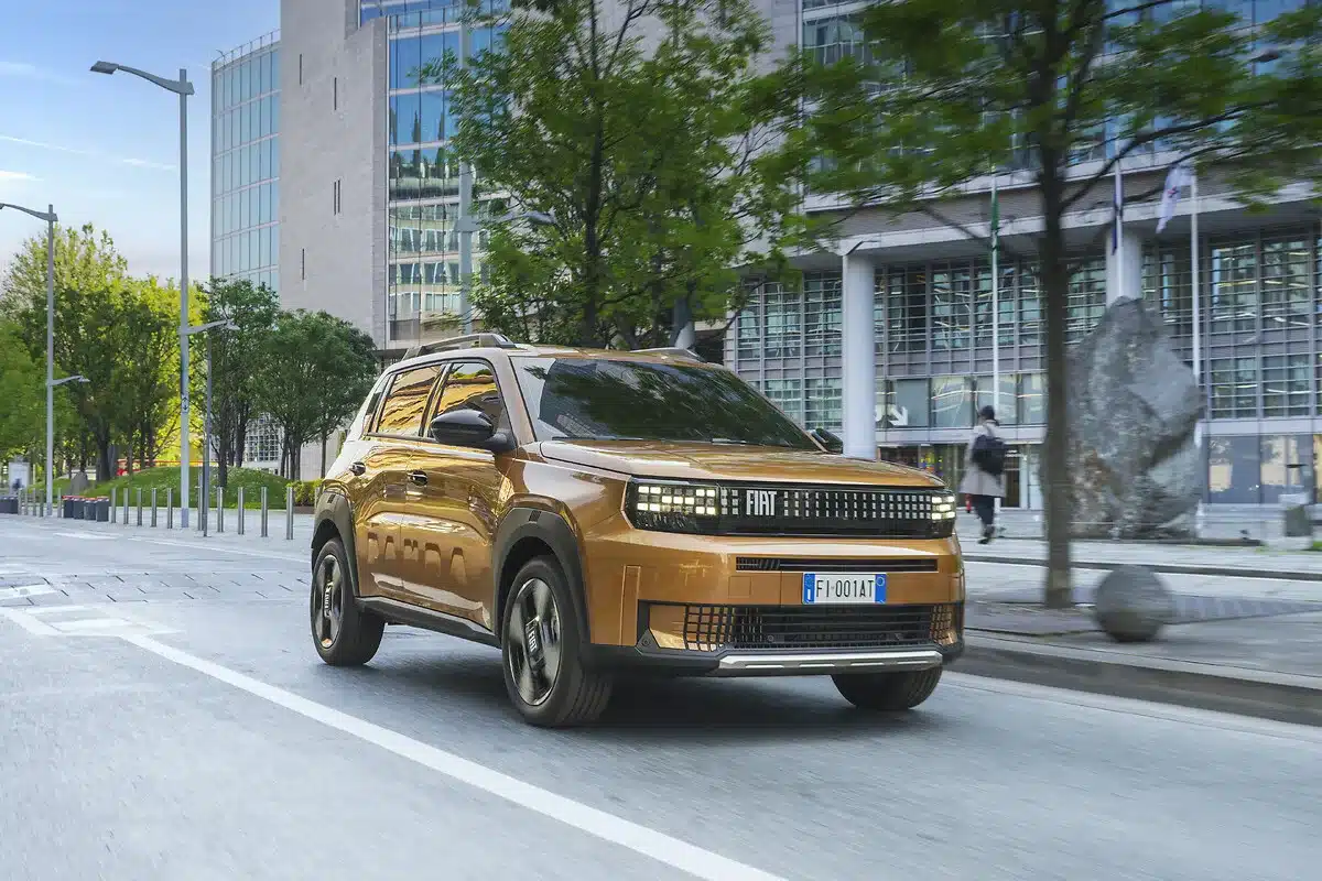 Fiat Grande Panda 2026 in Gold fährt auf einer Straße durch eine urbane Umgebung.