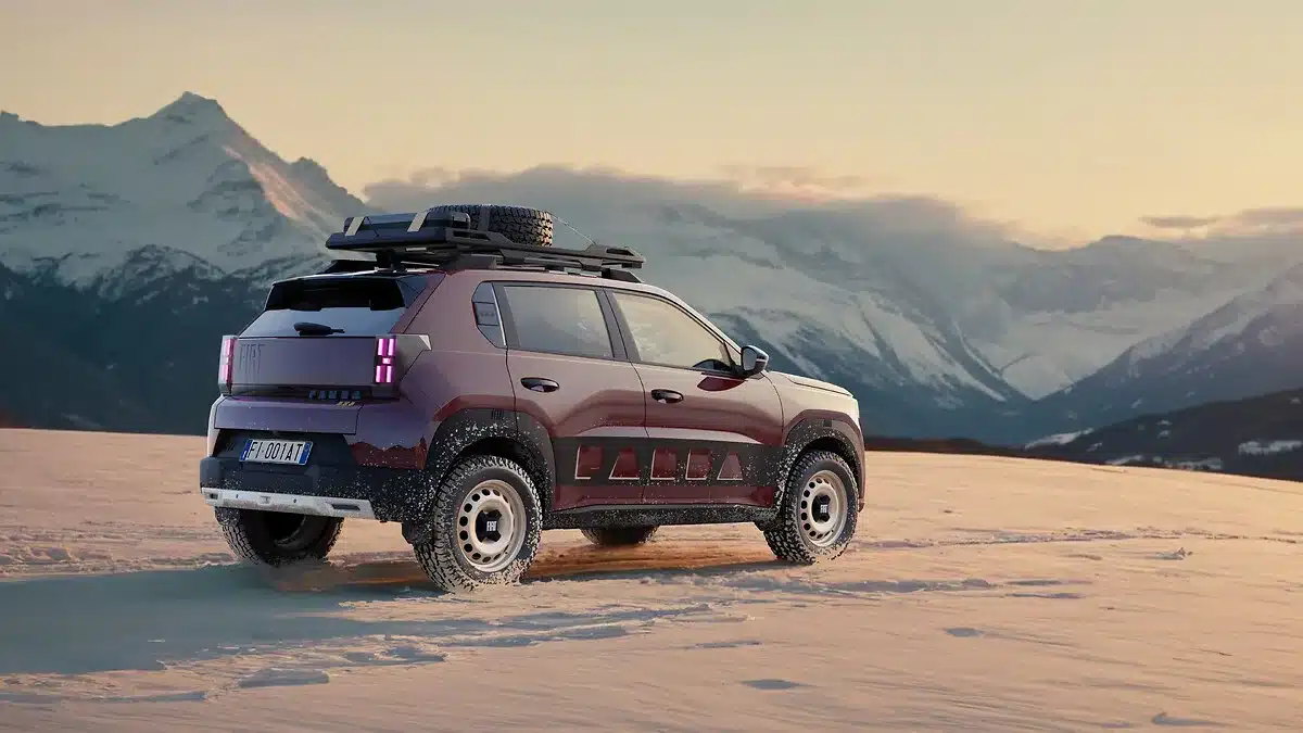 FIAT Grande Panda 4x4 in dunkelroter Lackierung mit Dachträger und Zusatzscheinwerfern auf Schneefeld vor Bergen.