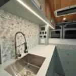 Küchenzeile mit Edelstahlspüle, Wasserhahn und danebenliegendem Stauraum im Ford Transit Bon Echo Campervan