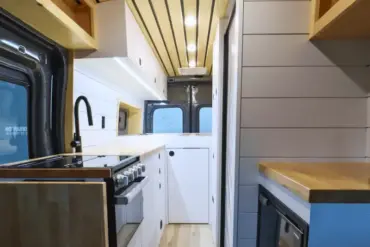 Innenansicht eines Campervans auf Ford Transit Basis mit moderner Bordküche, weißem Ausbau und Holzdetails.