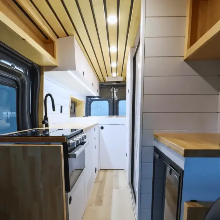 Innenansicht eines Campervans auf Ford Transit Basis mit moderner Bordküche, weißem Ausbau und Holzdetails.