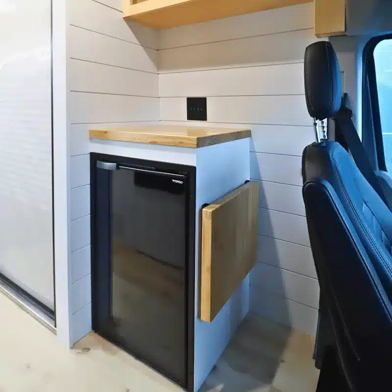 Nahaufnahme eines eingebauten Vitrifrigo C85 Kühlschranks mit Holzarbeitsplatte und ausziehbarem Seitentisch im Campervan.