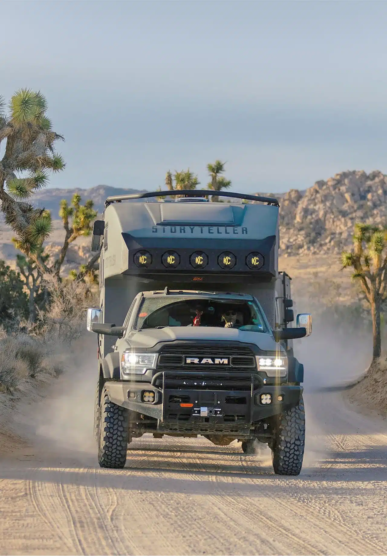 Der GXV HILT Adventure Truck fährt auf einer Offroad-Piste durch die Wüste, umgeben von Bäumen und Felsen