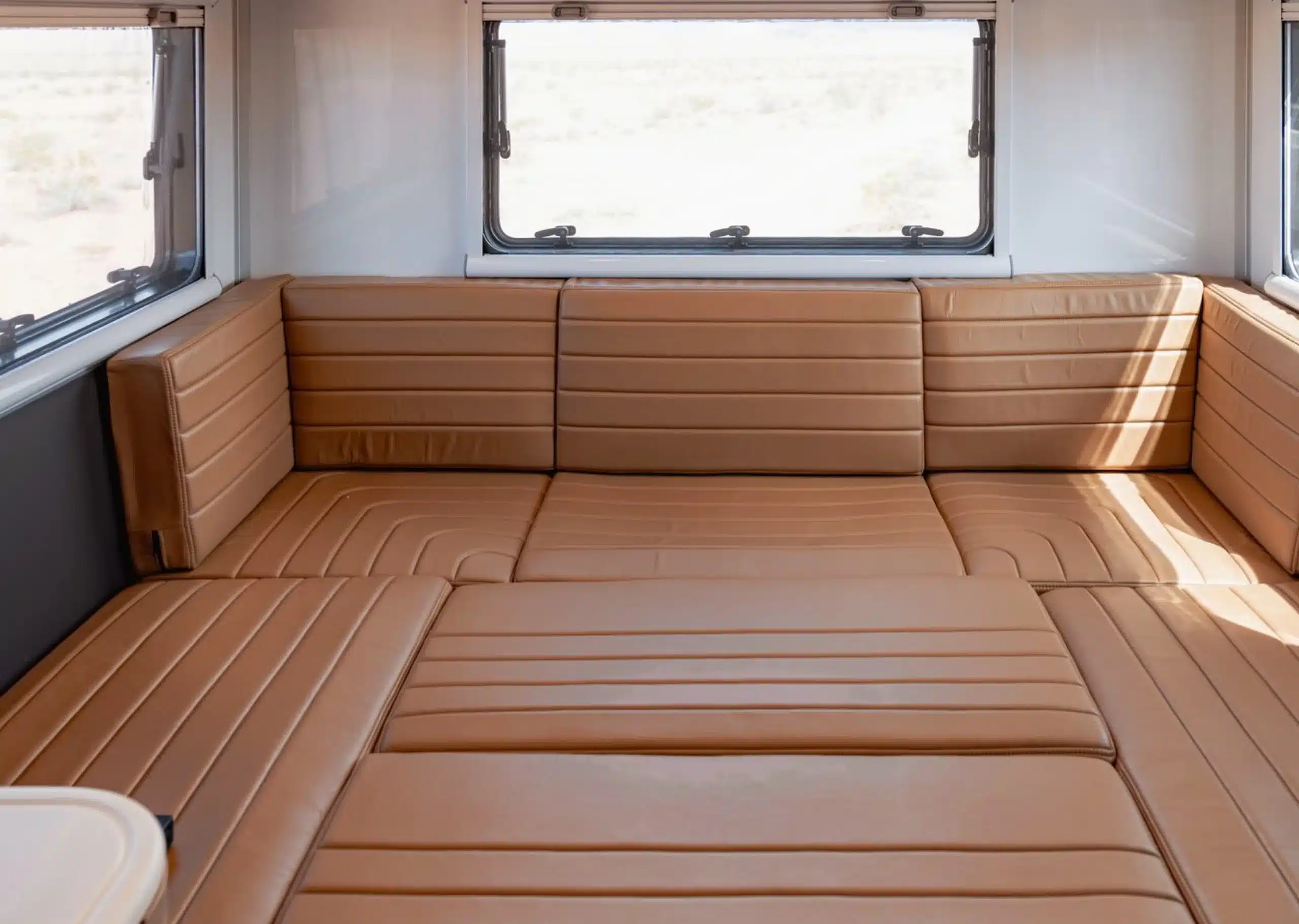 Der wandelbare Ess- und Schlafbereich mit hellbraunen Lederpolstern im GXV HILT Expeditionsmobil, umgeben von großen Fenstern