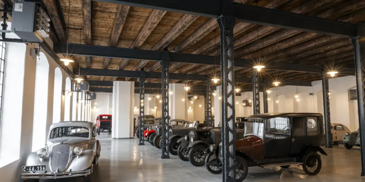 Ausstellung historischer Škoda-Fahrzeuge im Originalzustand in einer restaurierten Fabrikhalle mit sichtbaren Stahlträgern und Holzbalkendecke