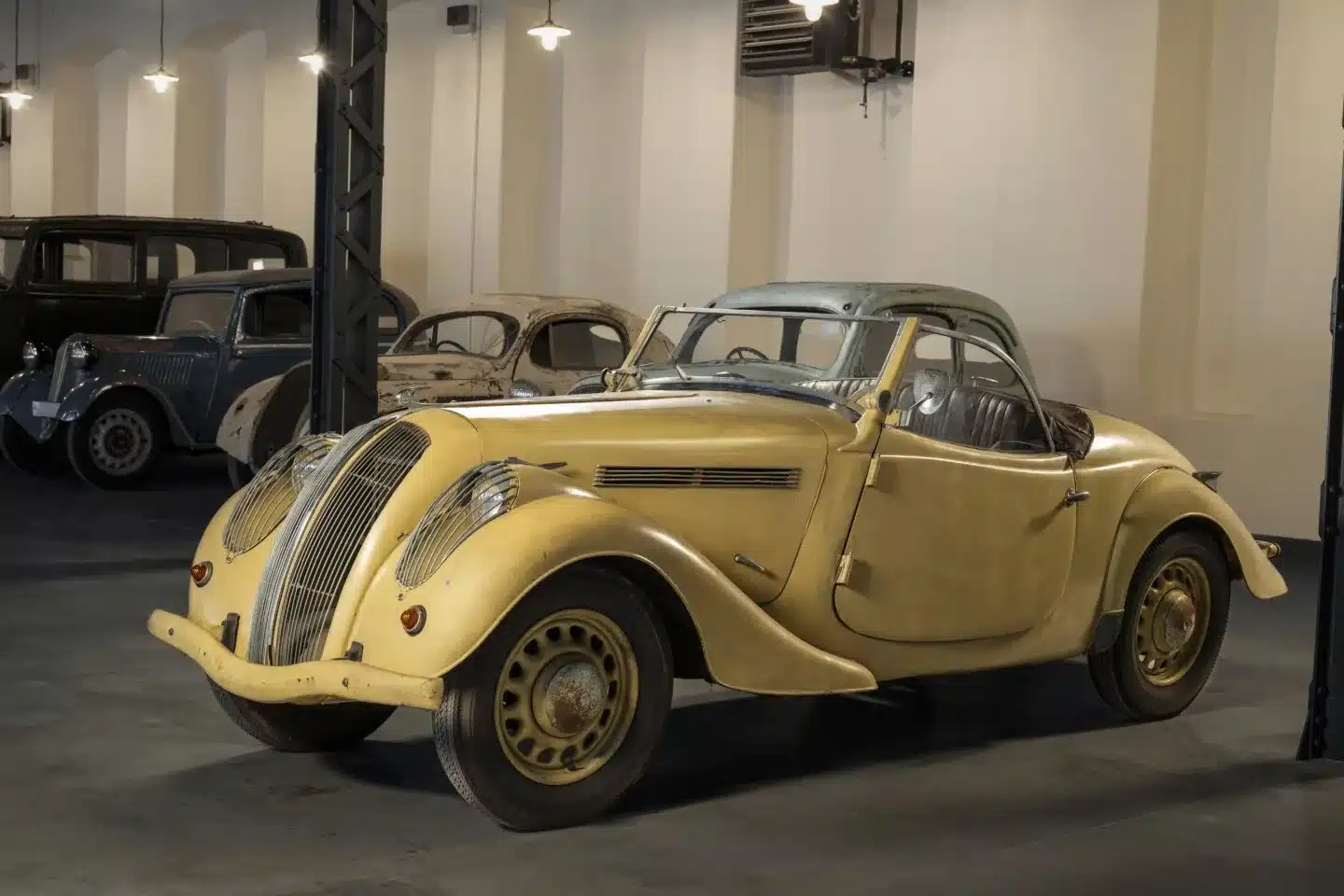 Historische Škoda-Oldtimer, darunter ein gelber Popular Monte Carlo Roadster, im Originalzustand in einer restaurierten Fabrikhalle ausgestellt