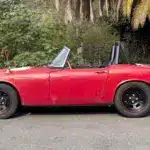 Roter Honda S600 Roadster von 1964 aus der Seitenansicht, unrestauriert, mit sichtbaren Gebrauchsspuren.
