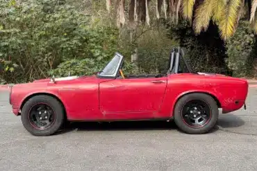 Roter Honda S600 Roadster von 1964 aus der Seitenansicht, unrestauriert, mit sichtbaren Gebrauchsspuren.