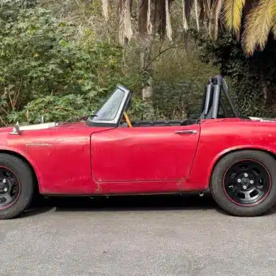 Roter Honda S600 Roadster von 1964 aus der Seitenansicht, unrestauriert, mit sichtbaren Gebrauchsspuren.