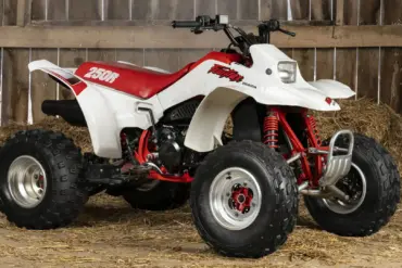 Honda TRX250R Fourtrax 1989, weiß-rot, in einer traditionellen Holzscheune auf Stroh stehend