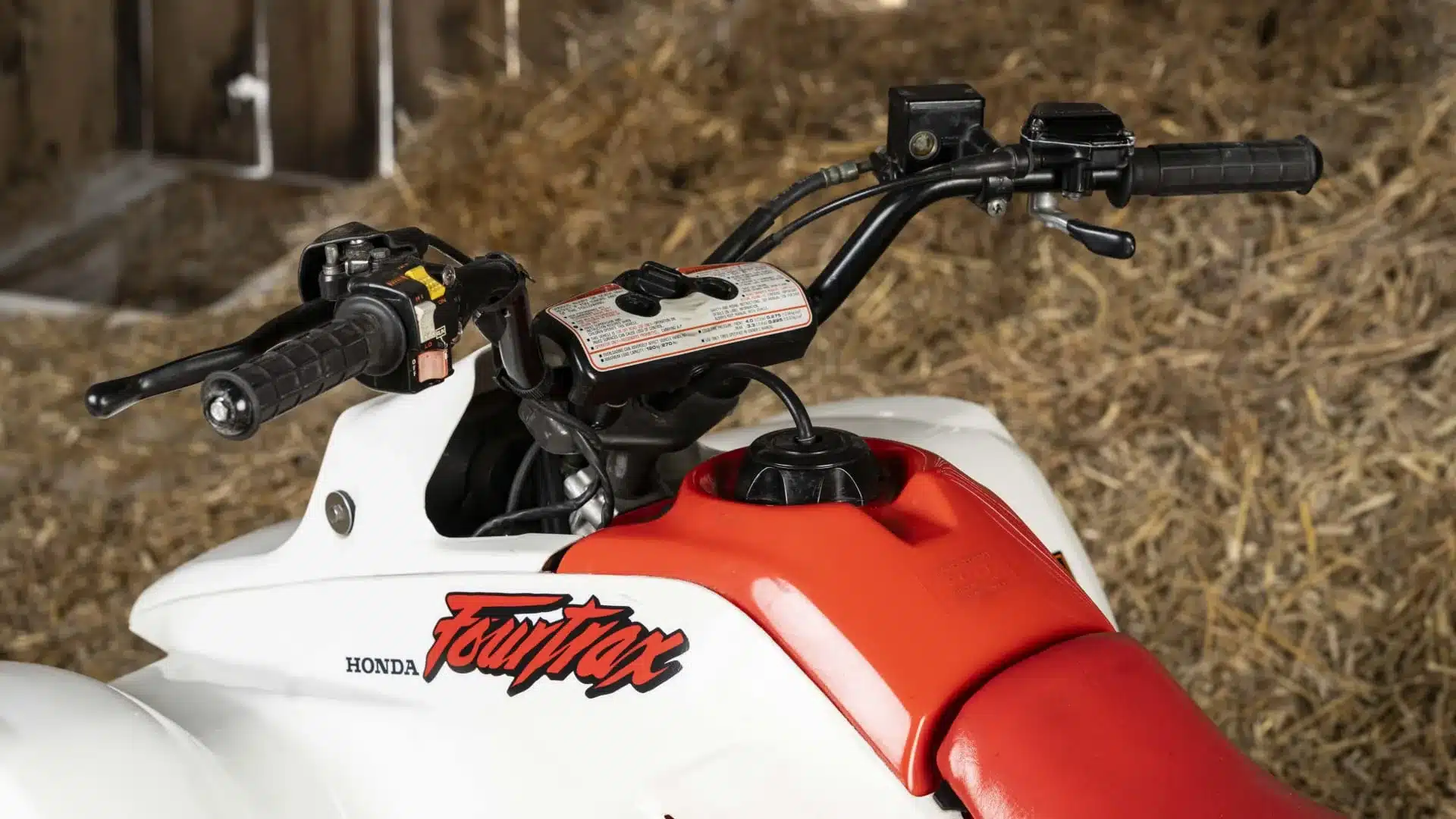 Lenker, Tank und roter Sitz einer weißen Honda TRX250R Fourtrax Baujahr 1989, fotografiert aus der Nähe.